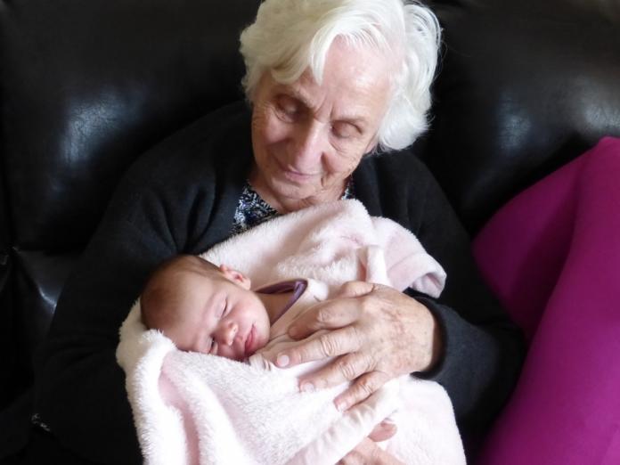 En ældre kvinde sidder med et spædbarn i armene. 