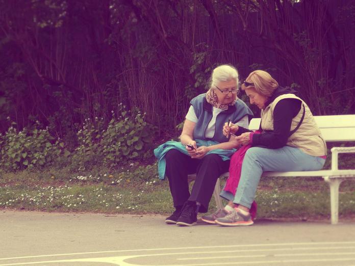 To kvinder sidder på en bænk og snakker. 