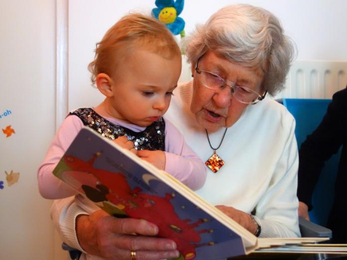En ældre kvinde sidder og læser i en bog sammen med et barn. 